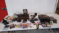 Overview of console, controllers, power supply, game cartridge stacks, manuals and assorted toys on table