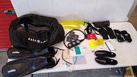 Photo showing all scuba gear items including fins, dive computer with console, gloves, weight belt, water shoes, and Aqua Lung dive bag laid out on table