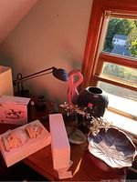 View of table top with desk lamp, pink flamingo decoration, dark blue vase, leaf platter, faux plant, and boxed drones.