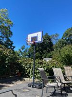 Side angled view of the basketball hoop showing the base, pole, and backboard with net attached outdoors on a paved area.