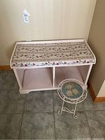 Wooden bench with two cubbies and floral cushioned removable pad on top, positioned on tiled floor.