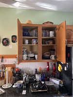 Kitchen cabinet with various kitchen items including blenders, coffee pots, mugs, plates, and glasses.