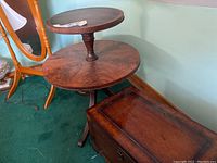 Photo of the two-tiered wooden accent table with circular tops and the wooden chest beside it, showing positioning and wear.