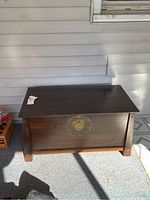 Front view of a rectangular wooden chest with dark finish and a large round brass plate in the center.