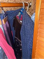 View of women's clothing including blue plaid jacket, brown dark top with floral pattern, and red dress hanging on a rod in a closet