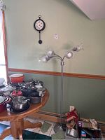 Full view of the floor lamp and wall clock mounted on green wall near a wooden table with cookware.