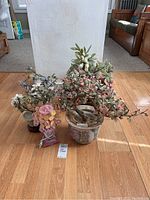 Five glass floral arrangements in decorative pots on wooden floor with a white wall background.