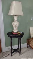 Full view of the oval carved wood table with the vintage ceramic lamp on top, positioned against a green wall, showing lamp cord and seating area nearby.