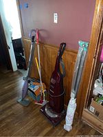 Full view of Kenmore vacuum cleaner, Shark Swiffer mop, and packaged lightbulbs standing against wall with wooden paneling and hardwood floor.