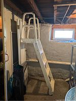 Full view of the white plastic pool ladder standing upright indoors, near a door and window.