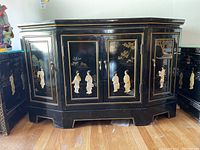 Front view of Asian inspired black lacquered sideboard with carved inlay figures and landscape motifs on cabinet doors and sides.