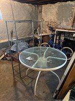 Photo showing the 4-tier metal storage rack and round glass-top table in a basement or garage.