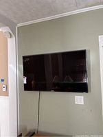 Front view of Samsung TV mounted on wall with visible power cord.