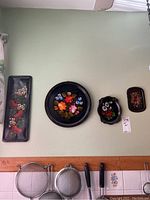Four pieces of metal wall art mounted on a wall above kitchen utensils, showing variety of floral designs and shapes.