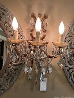 Front view of antique style crystal wall sconce mounted on wall with three lit bulb arms and hanging crystal prisms.