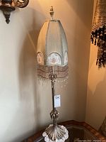 Full view of antique style table lamp showing ornate metallic base and fringed fabric lampshade