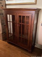 Front view of the medium brown solid wood Arts & Crafts style bookcase cabinet with two glass-paneled doors and wooden knobs.