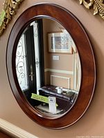 Full view of the classic oval wood framed mirror hanging on the wall, showing the overall shape and size with a 26x30 inches measurement tag.