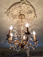 Overall view of lit chandelier showing decorative ceiling medallion and five candle-style lights