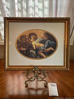 Overall view of framed angel cupid print on brass easel.