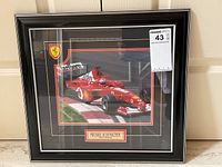 Angled view showing plaque reading “Michael Schumacher Team Ferrari,” frame edge and glass reflection.