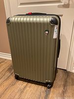 Front angled view of the gold hard case suitcase showing the full height, wheels at bottom, and textured ridged pattern.