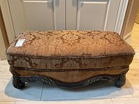 Front angle view of the rectangular gold damask fabric upholstered ottoman with carved wood base and legs, showing detailed upholstery and wood scrollwork.
