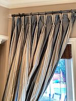 Two striped panels hanging from a dark metal rod with clear acrylic finials over a patio door