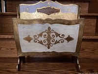 Front view showing hand-painted gold and cream ornamental pattern with carved handle on top rail and wood grain visible.