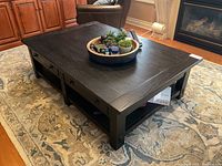 Angled front view of black wood coffee table showing four drawers, open shelves, and top surface with decorative tray.