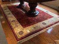 Full view of burgundy area rug under dining table showing border and fringe