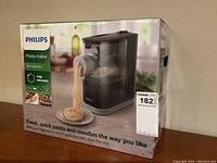 Front of sealed retail box showing machine extruding noodles and box art