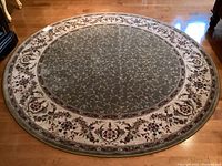 Full view of round sage green carpet with floral border on wooden floor.