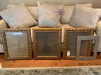 Three large faux bamboo textured picture frames with golden brown finish arranged on floor in front of couch. One frame includes matching removable taupe matting.