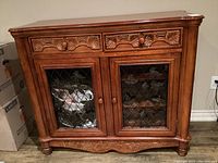 Full view of solid wood carved cabinet with two drawers and two glass-front doors with wrought iron grape vine designs.