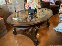 Full view of oval coffee table showing wood frame, glass top, and wrought iron base