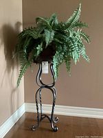 Full view of the wrought iron plant stand with artificial fern in terracotta planter against wall.