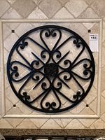Front view of the wrought iron wall decor laid flat on a tile surface, showing circular design with hearts and scrolls.