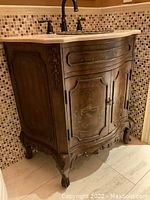 Angled front view of entire vanity showing carved wood doors, painted urn design, granite top and faucet.