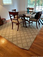 Beige area rug with diamond pattern under wooden dining table and chairs, corner view showing edges and floor transition