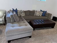 Front left view of grey sectional with chaise, tufted cushions, decorative pillows, and leather ottoman