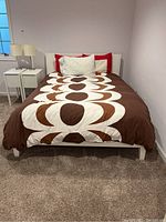 Bed fully made showing white Ikea bed frame with brown and white Marimekko duvet cover and pillows arranged on top.