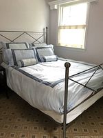 Bed made with white comforter and light blue bordered pillow shams, showing entire bed setup.