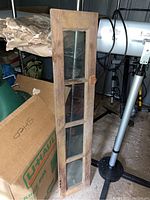 Photo of a narrow wooden cabinet door with four vertical glass window panels showing weathered wood and rust on hardware.