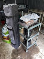 Gray canopy bag standing upright beside a metal shelving unit with weights and supplies.