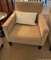 Front view of beige Crate and Barrel armchair with light patterned beige accent pillow placed on seat cushion. Dimensions roughly 32x32x34 inches.