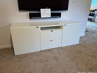 Front view of white IKEA credenza showing two cabinet doors on sides and two drawers in center with glass top visible.