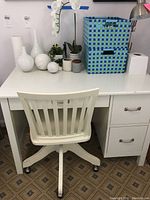 Full view of white student desk beside matching rolling chair, items arranged on the desk surface including vases and a lamp.