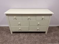 Front view of the white wood dresser showing seven drawers with round knobs and visible scratches on the surface.