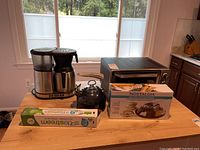 Wide shot showing all items on wooden table including the coffee maker, teapot, toaster oven, s'mores maker box, and Sodastream cartridge box.